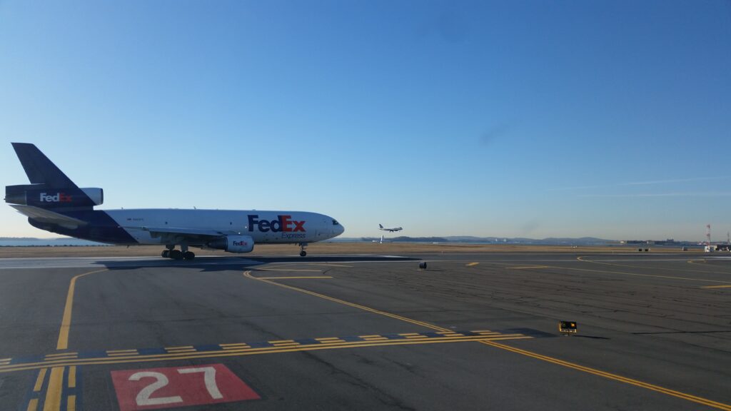 Fedex getting ready to takeoff in Boston while an Embraer lands in the background on a different runway.